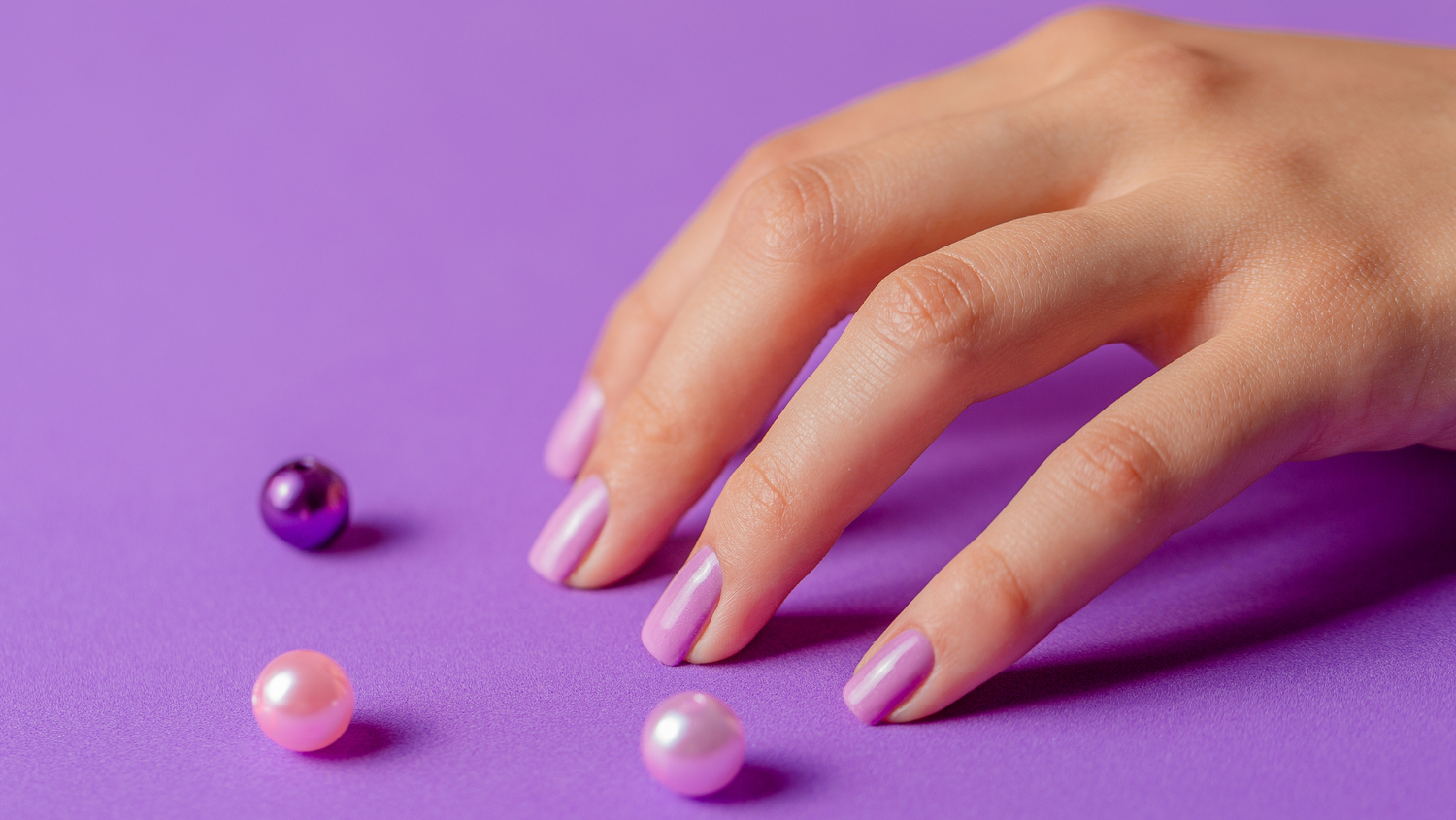 Close-up of a hand with elegant lavender gel polish on a purple background, surrounded by decorative loose pearls.