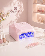 A soft pink GuguSure UV LED nail lamp sitting elegantly on a manicurist workstation equipped with premium nail accessories and top coats. This highly efficient professional nail drying machine is engineered to significantly speed up curing times for gel nails while maintaining a chic, professional look that perfectly complements any modern nail salon decor or mobile nail tech's essential toolkit.