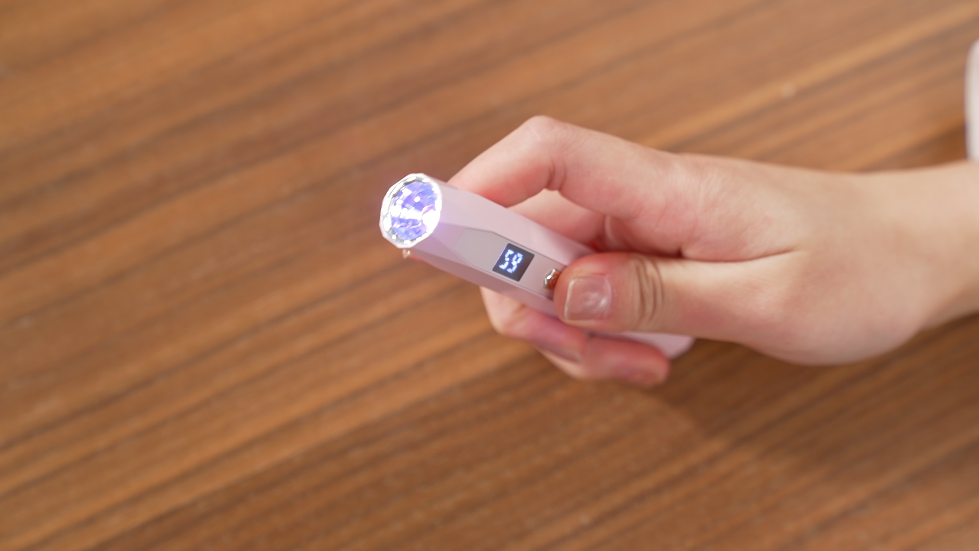 Illuminated pink Gugusure portable mini flash cure light pen over a wooden desk.